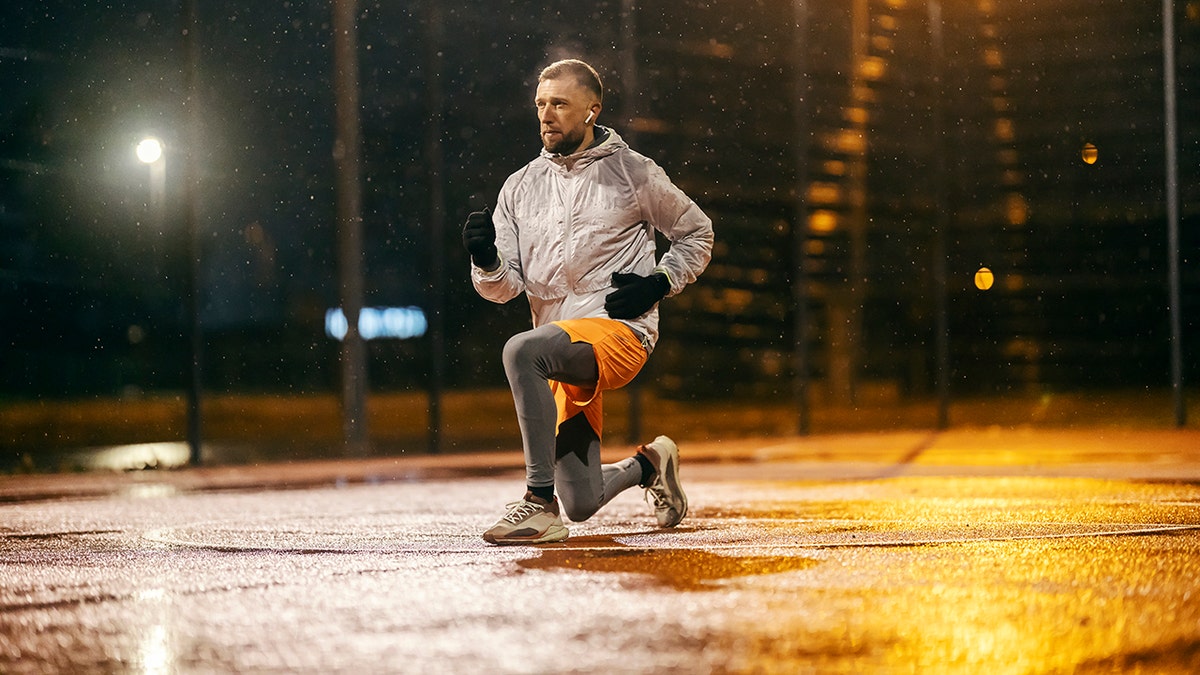 Fit young man working out outside in cold, wearing gloves and earbuds.