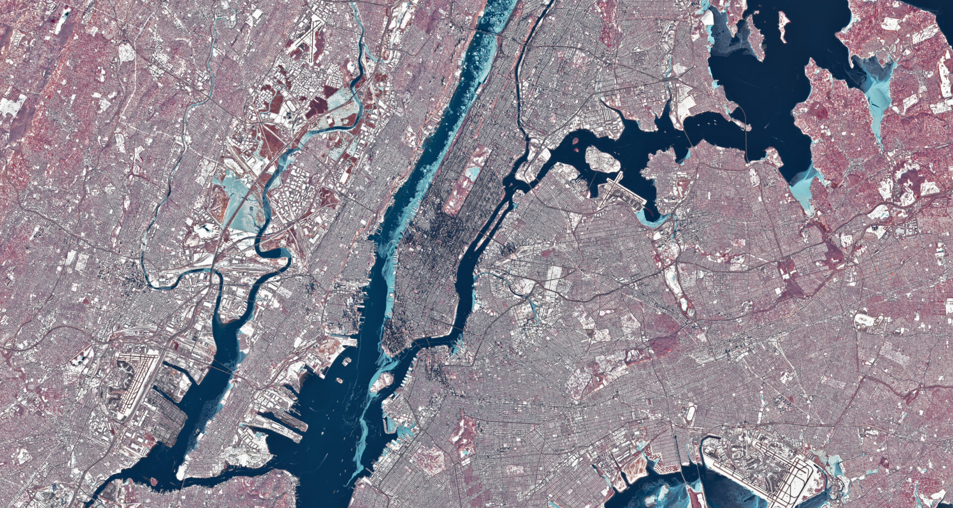 Chunks of ice, which appear light blue in this false-color image, line the western shore of Manhattan in the Hudson River. Smaller rivers and lakes in the scene also appear frozen or partially frozen. The ground is snow-covered, and tall buildings cast long, dark shadows.