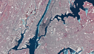 Chunks of ice, which appear light blue in this false-color image, line the western shore of Manhattan in the Hudson River. Smaller rivers and lakes in the scene also appear frozen or partially frozen. The ground is snow-covered, and tall buildings cast long, dark shadows.