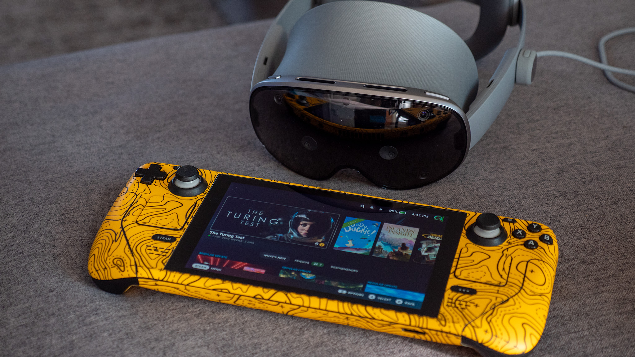 A Samsung Galaxy XR next to a Steam Deck wearing a yellow Dbrand skin