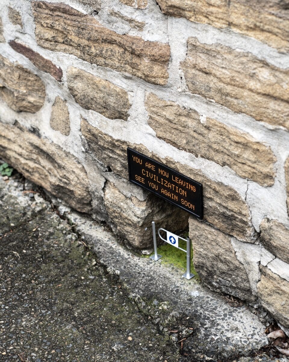 A miniature installation by Michael Pederson of a gap at the base of a stone wall with a gate and a replica digital sign that reads