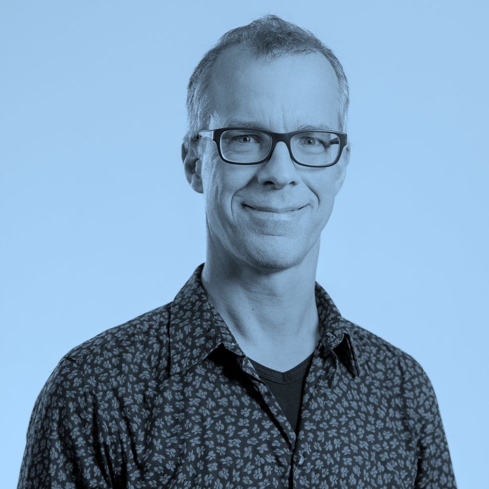 Person wearing a patterned shirt against a pale blue background.