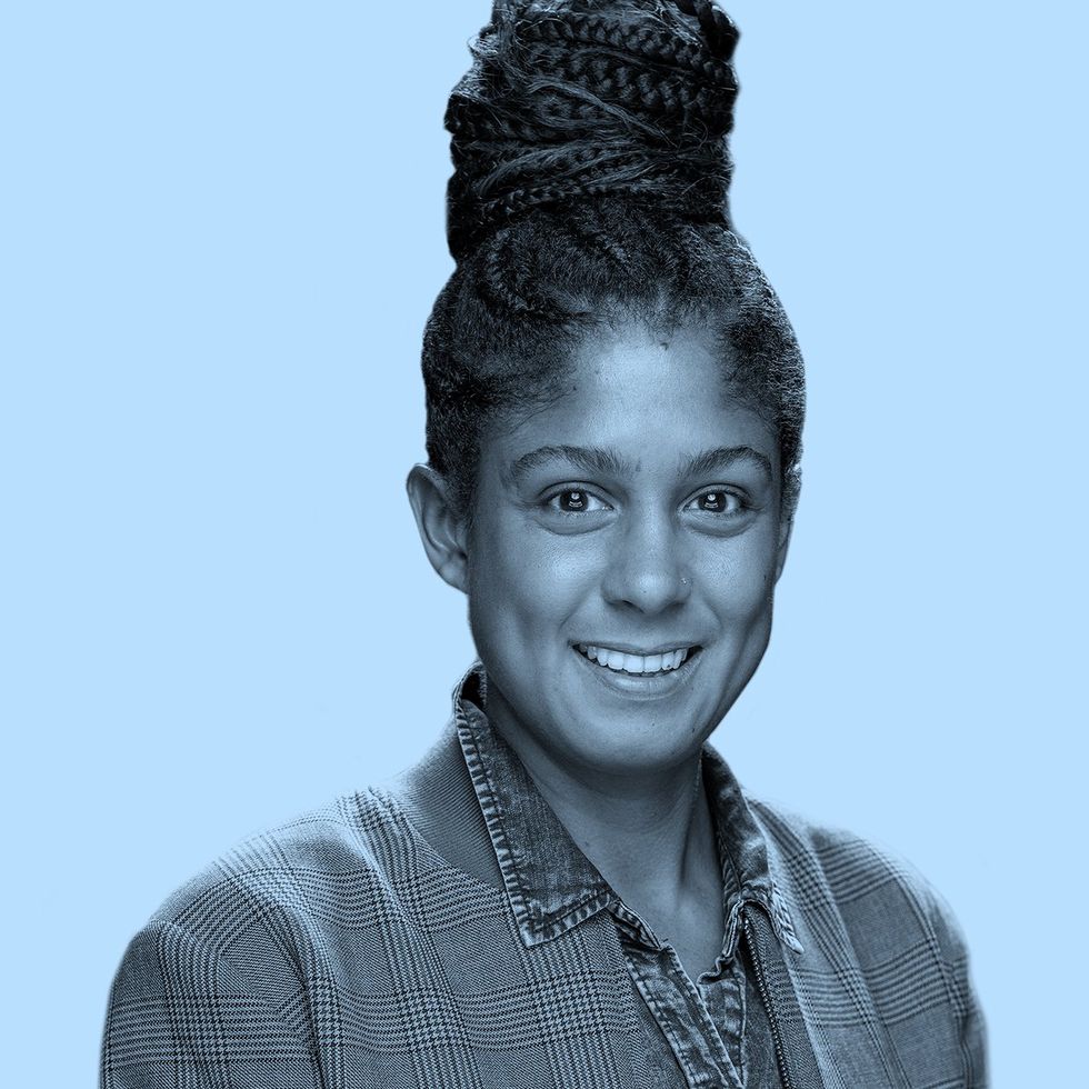 Person with braided updo in checkered suit jacket and chambray shirt, light blue background.