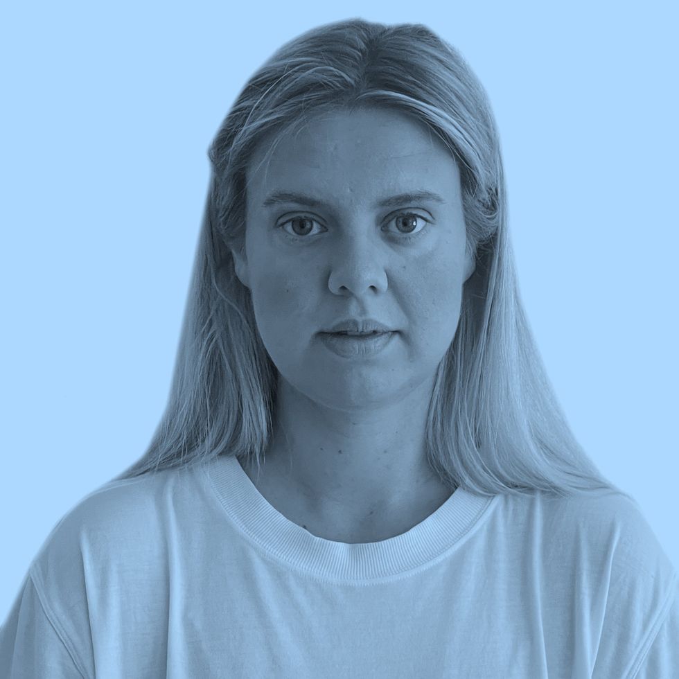 Person with long blonde hair in a white shirt against a solid blue background.