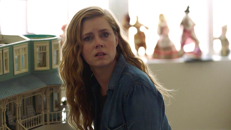 Camille crouches next to a dollhouse in 