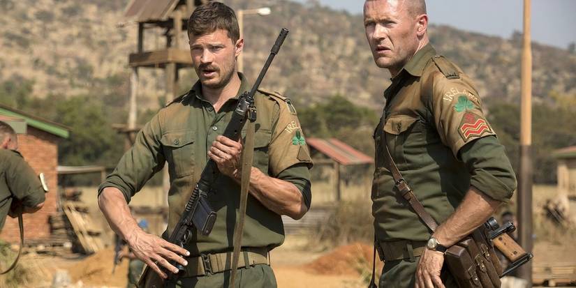 Two Irish soldiers stand in a military installation. The one on the left has a raised rifle. 