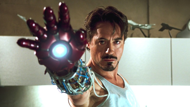 Robert Downey Jr. as Tony Stark holding out his arm with a red mech glove on it in Iron Man