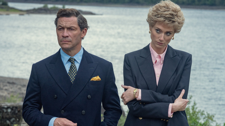 Prince Charles (Dominic West) stands grimly next to Princess Diana (Elizabeth Debicki) near a river in The Crown