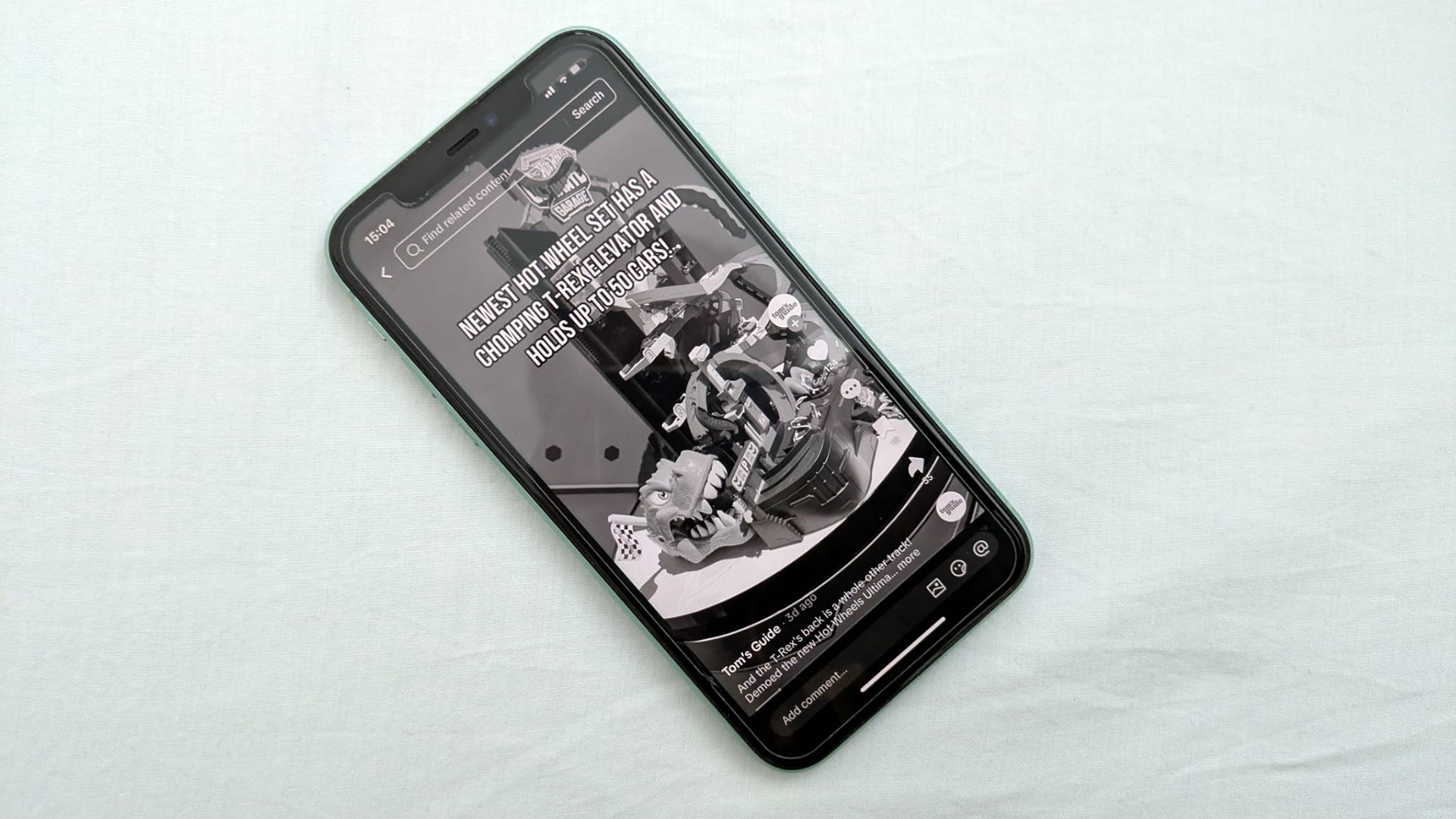 An image of an iPhone 11 against a pillow, showing the Tom's Guide TikTok page in grayscale
