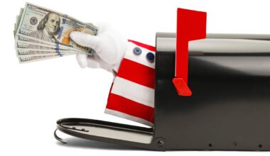 A hand in a white glove with a red-and-white sleeve extended from a mailbox while holding $100 bills.