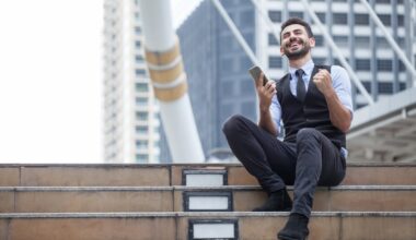 An investor cheers while sitting outside on steps.