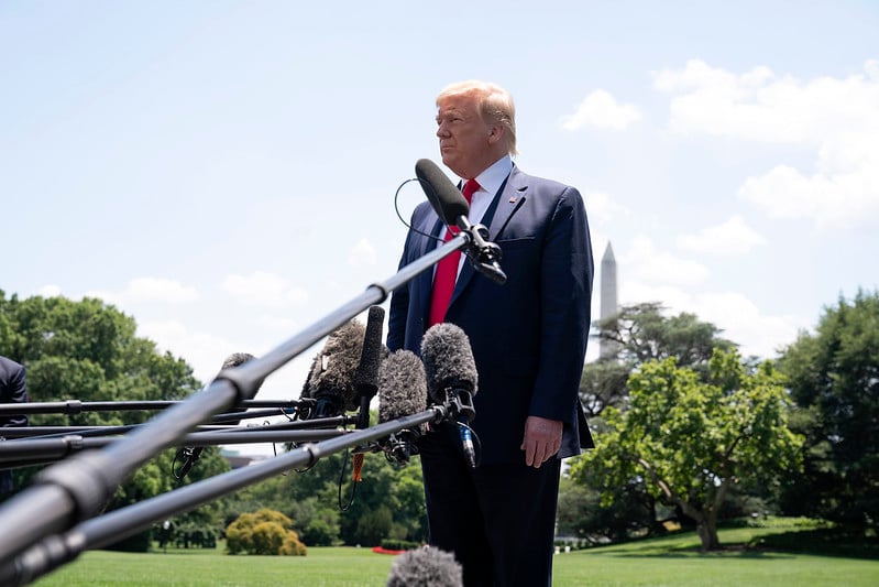 President Donald Trump standing behind   a microphone in an outdoor setting.