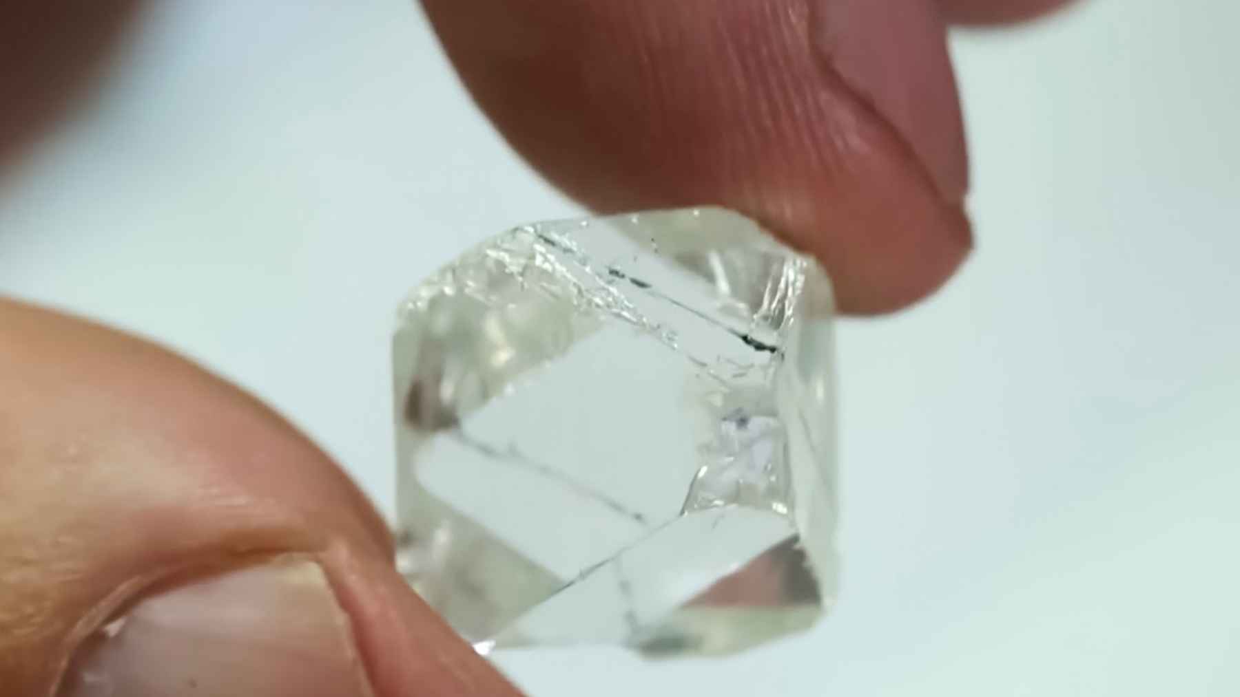 Synthetic diamond crystal held between fingers, symbolizing US-Japan plans to invest $550B to reduce reliance on China