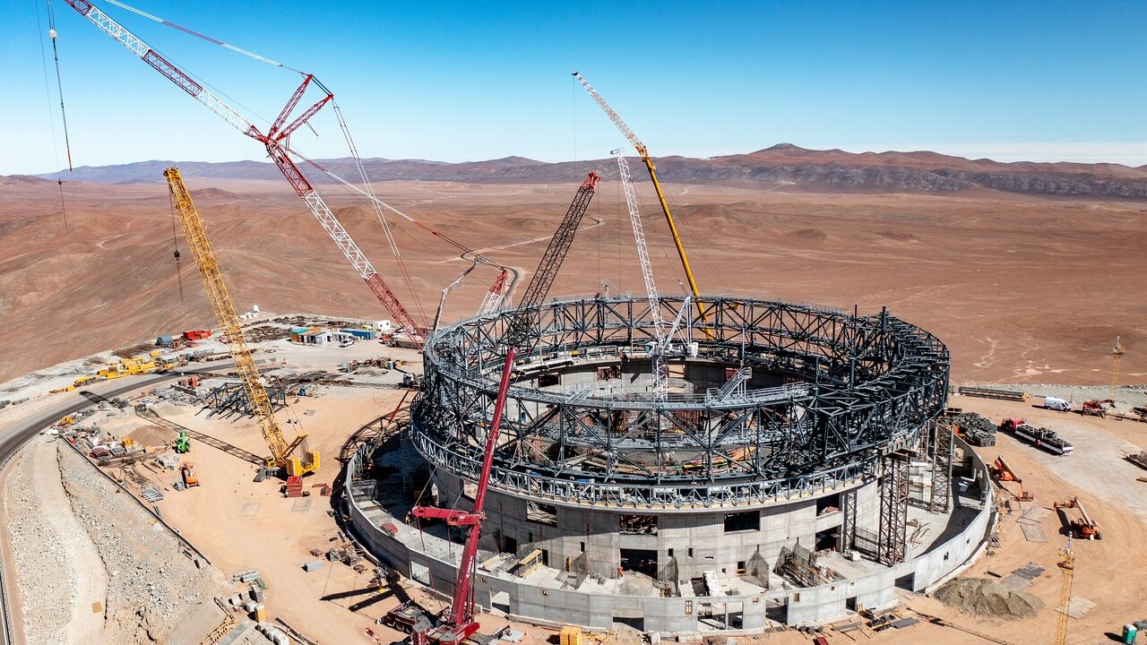 A spiral building of scaffolding sits in a brown, sandy desert.
