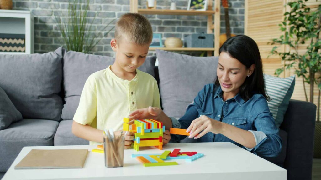 A woman and a boy playing with colorful wooden blocks at a table.