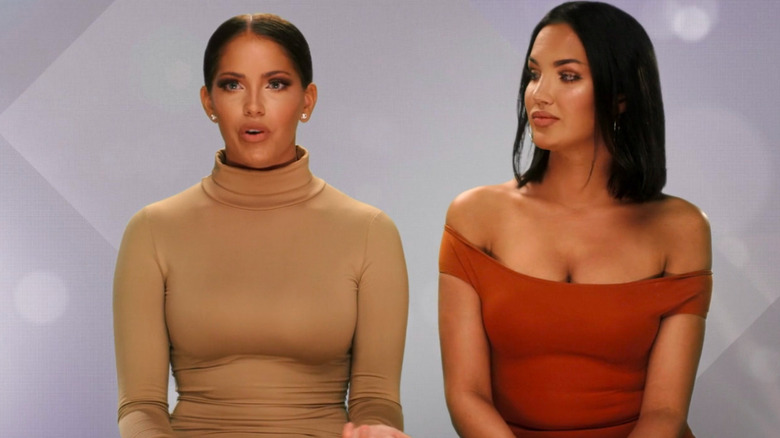 Olivia and Natalie sitting next to each other in confessional with white/grey background in WAGS