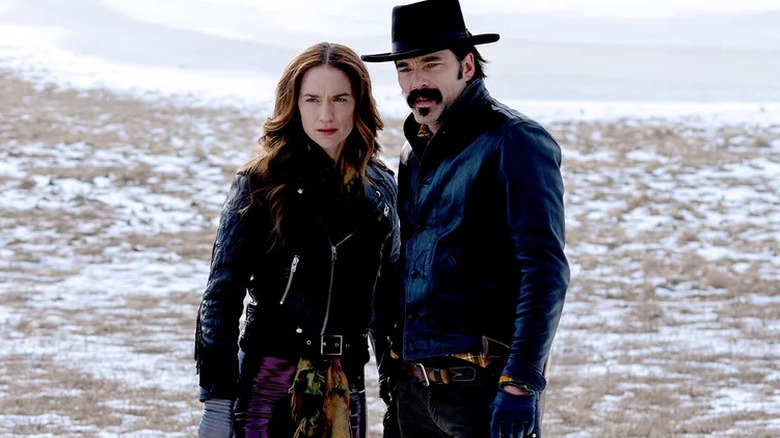 Melanie Scrofano as Wynonna in leather jacket on snowy field next to Tim Rozon as Doc Holliday in leather and black hat in Wynonna Earp
