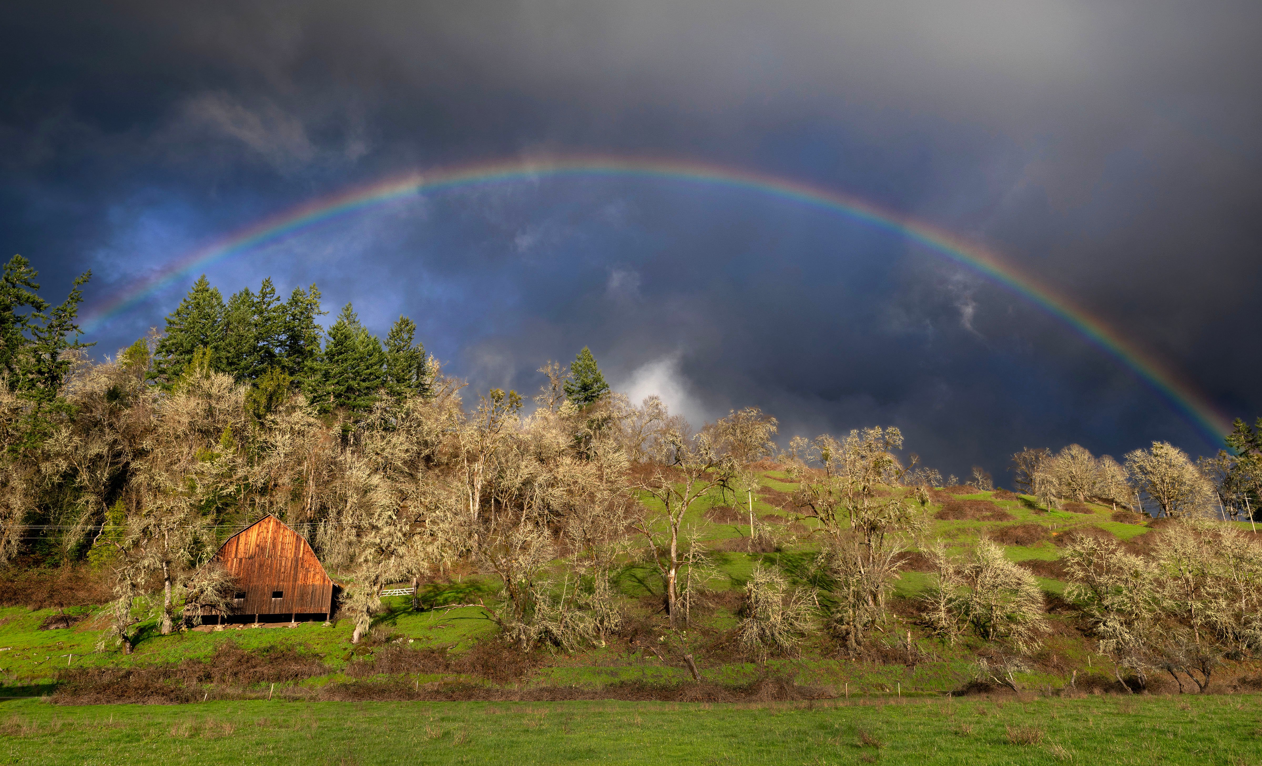 A rainbow arcs over a country barn on a hillside in Douglas County, Oregon.