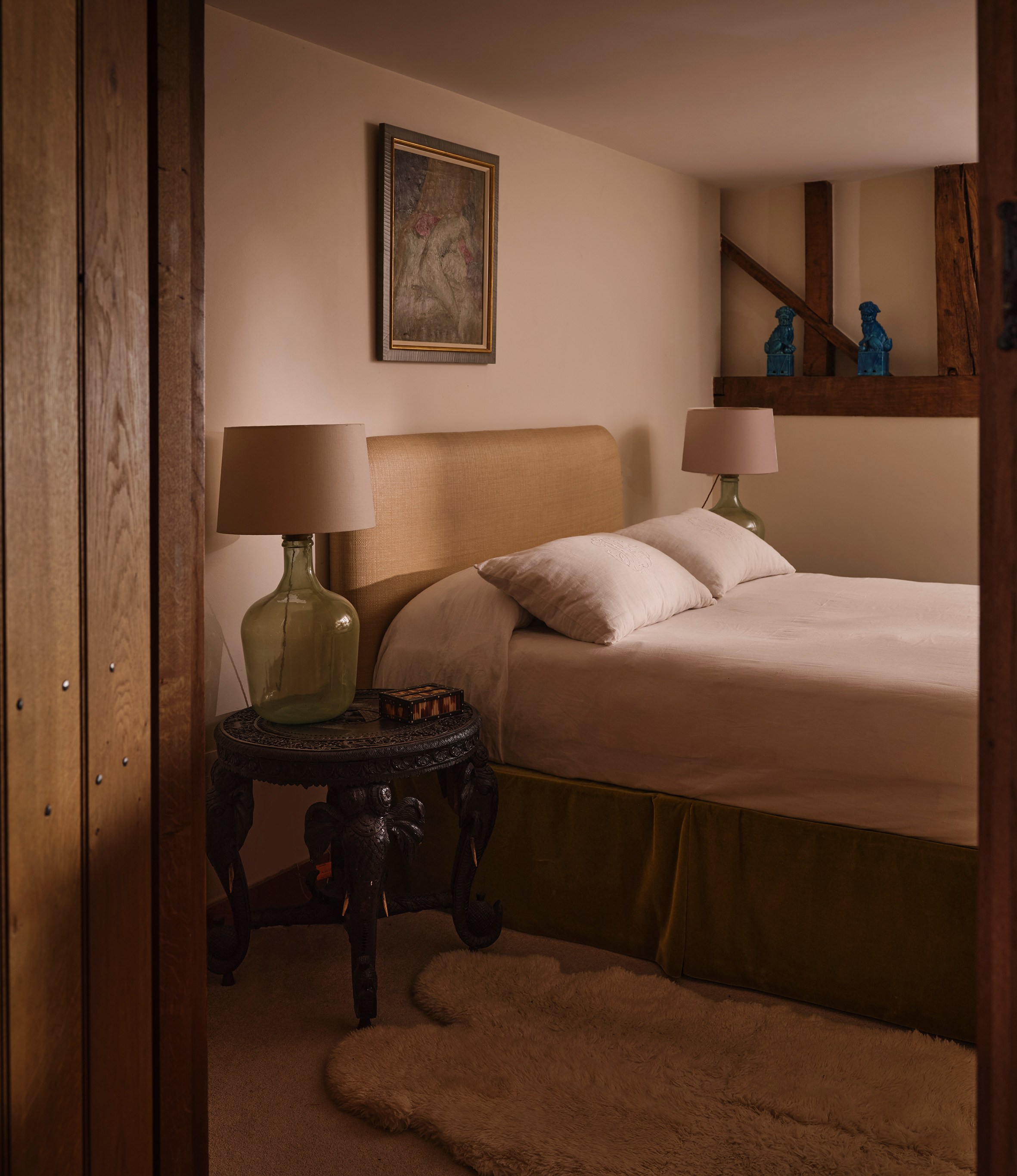 A cozy bedroom with a bed, two lamps, a painting, and a small table.