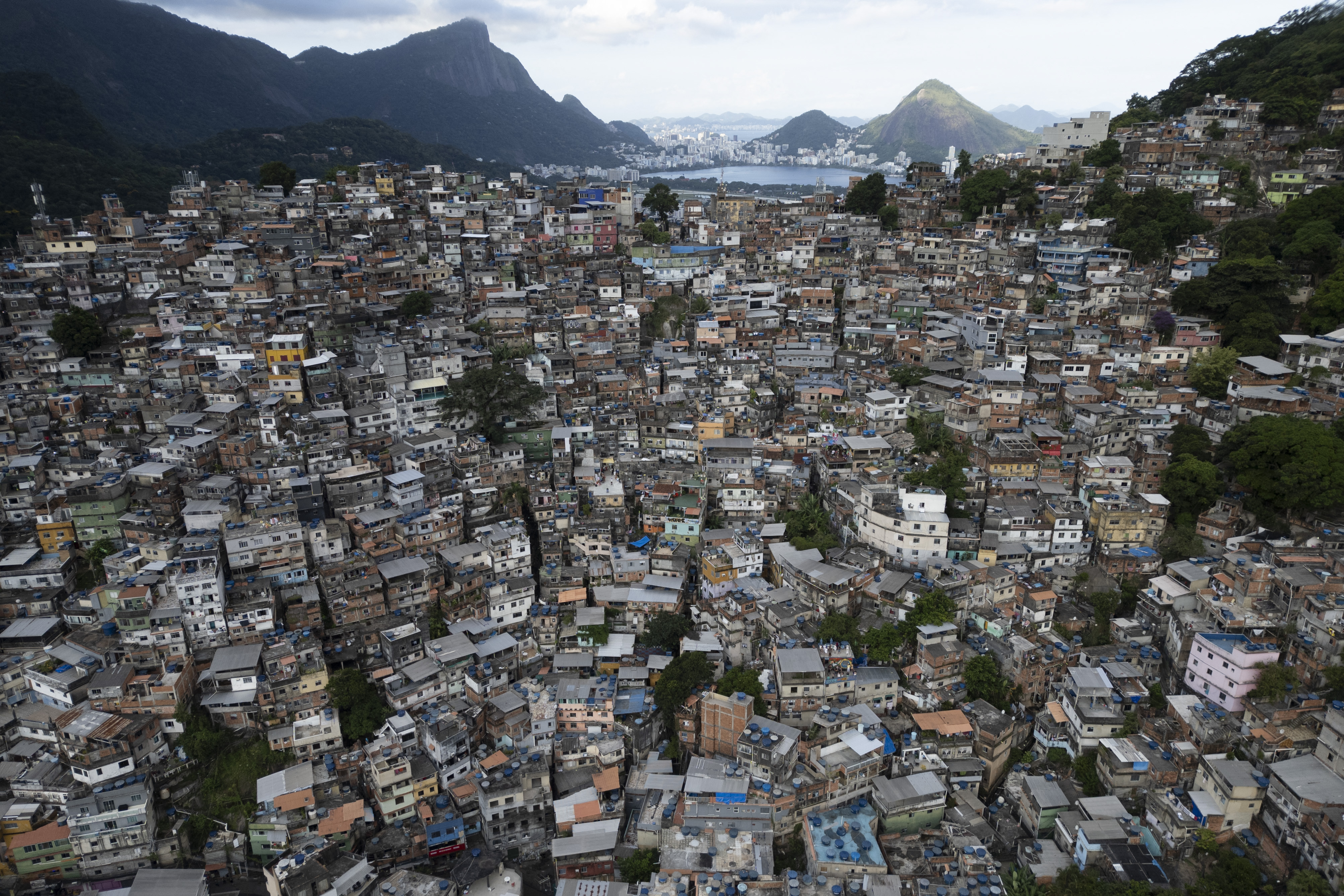 Aerial view of the Rocinha favela in Rio de Janeiro, Brazil, with densely packed homes on hillsides and mountains in the background.
