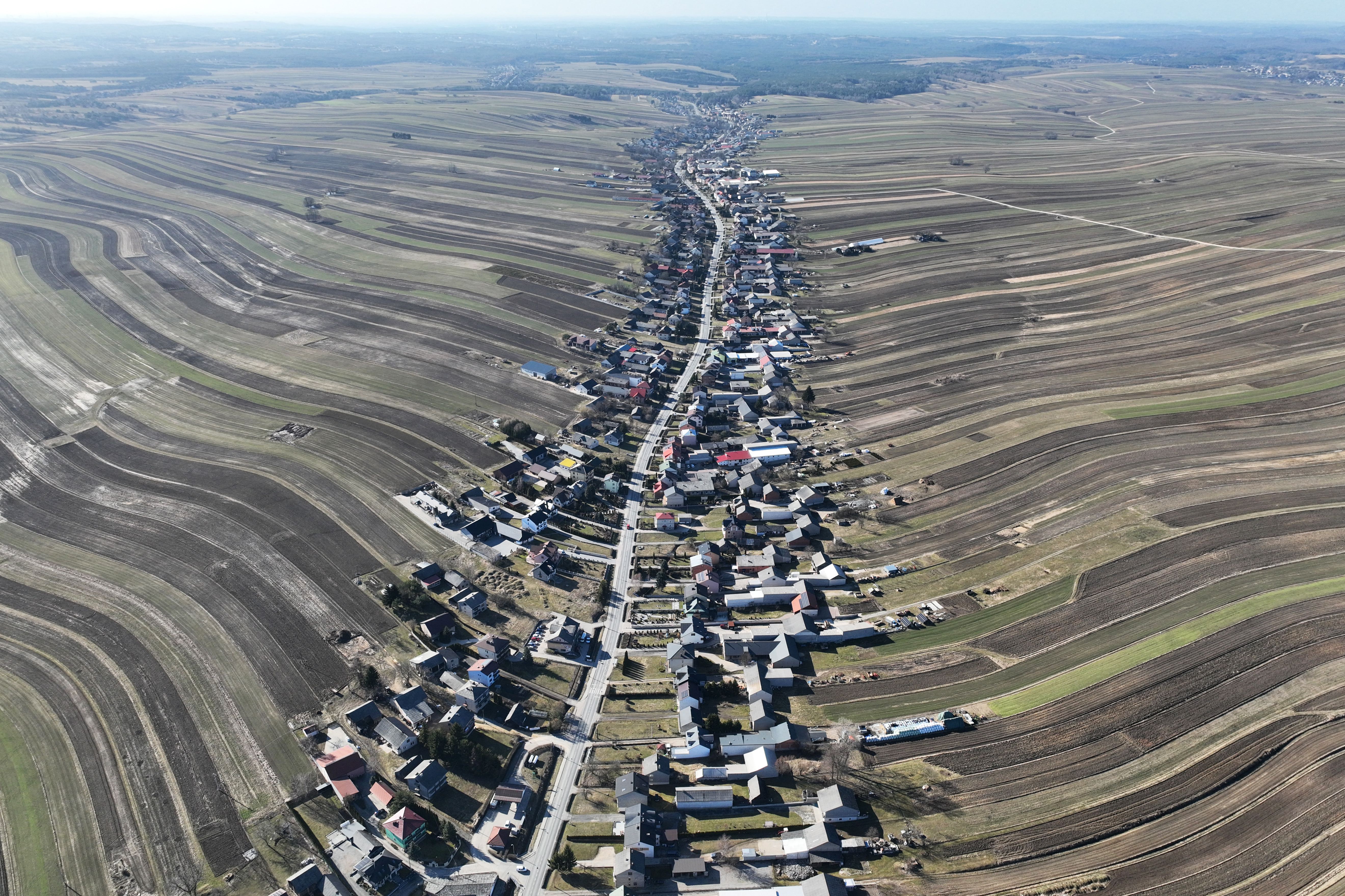 Aerial view of Suloszowa, a Polish village where houses line a 9-kilometer road, surrounded by wavy agricultural fields.