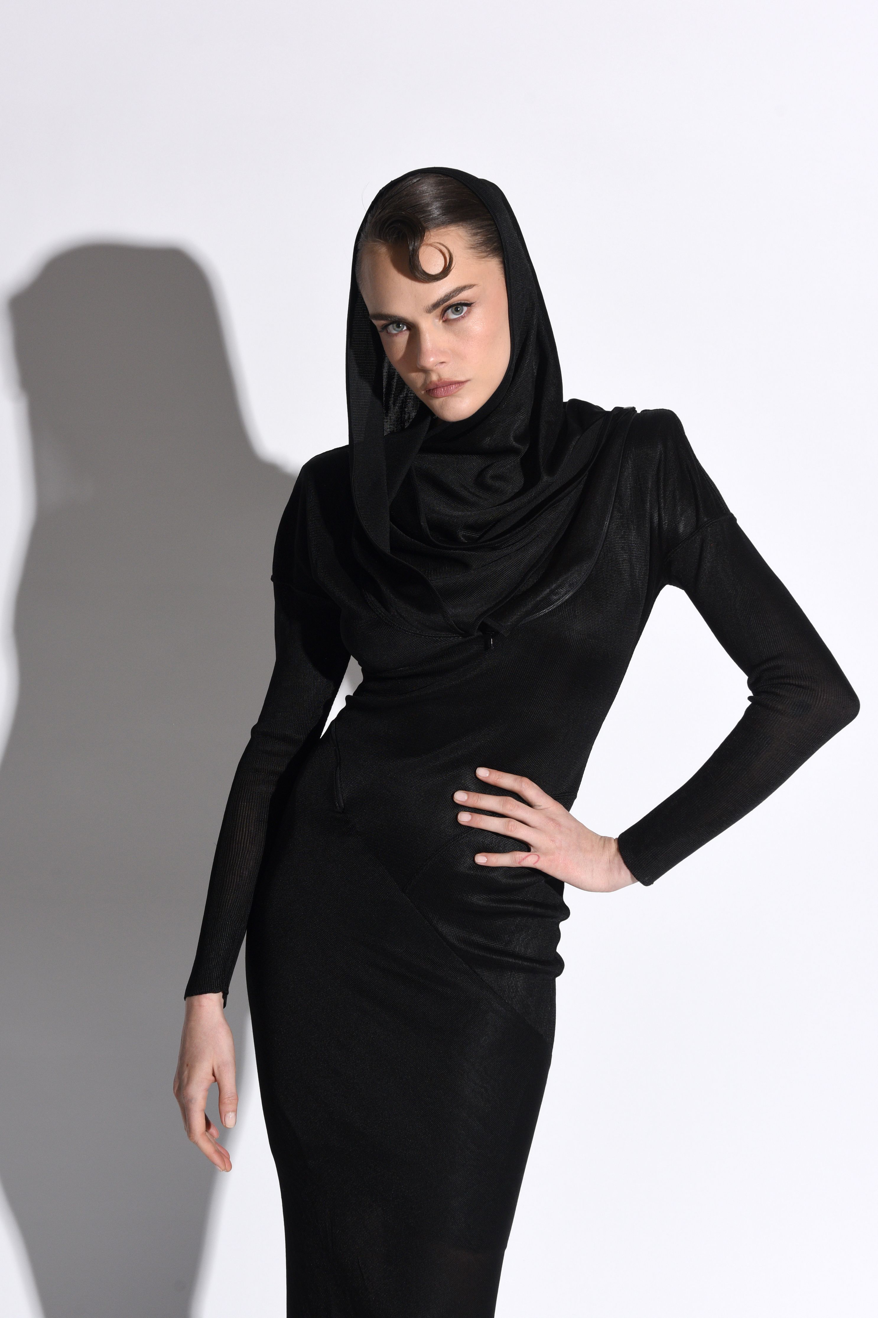 Cara Delevingne poses in a black dress and head covering.