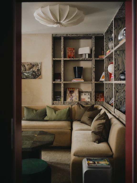 Cozy living room with a beige corner sofa, green throw pillows, and bookshelves filled with various items and books.