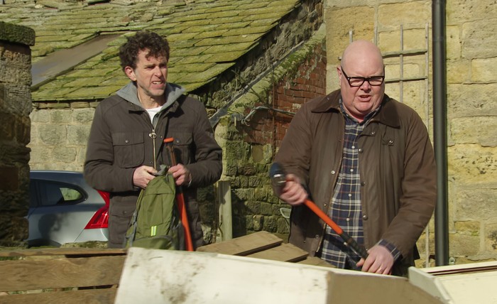 Paddy and Marlon stand outside of Celia's farm, armed with sledgehammers, in a scene from Emmerdale