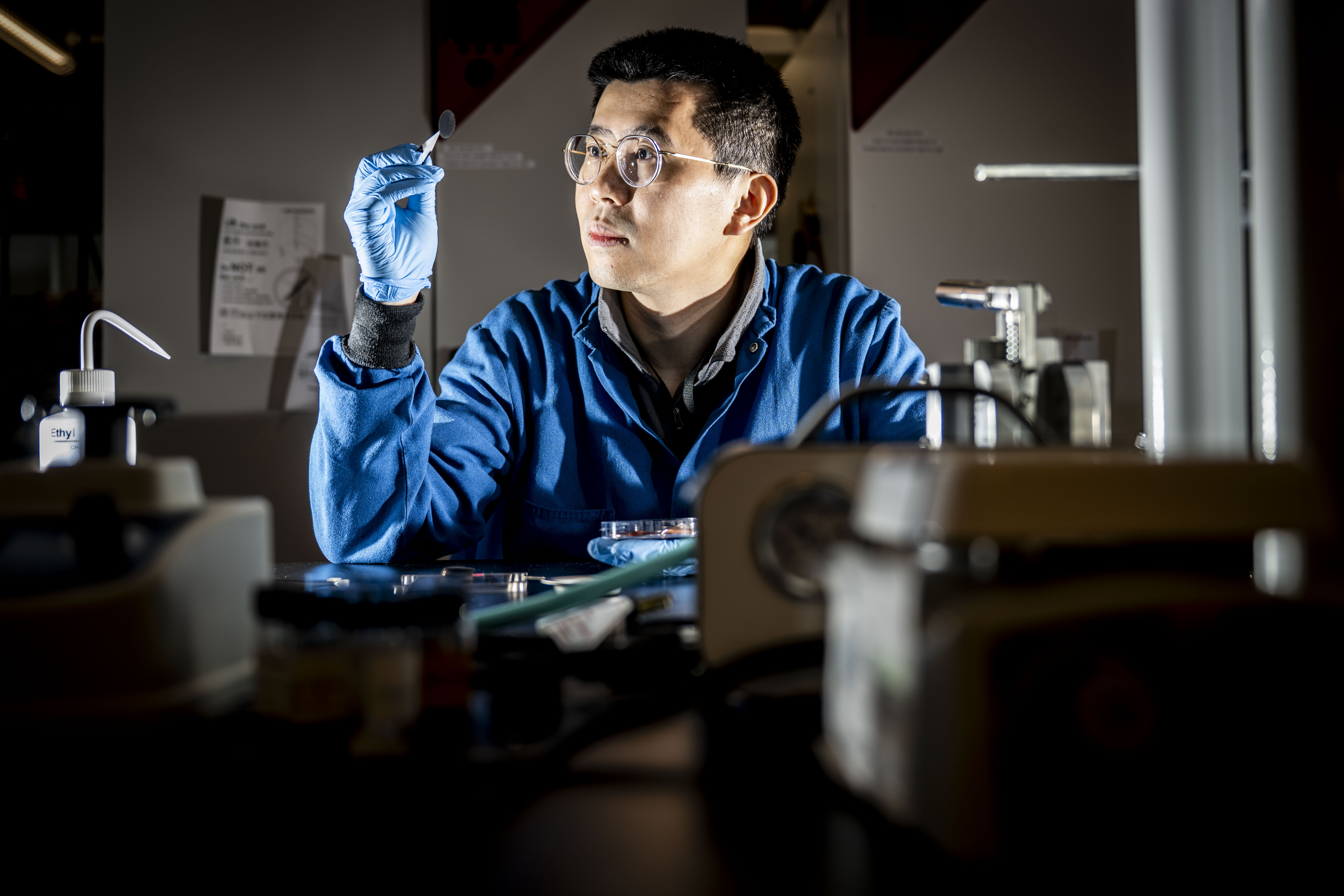 A researcher in a lab coat and safety glasses examines equipment while working on electric vehicle battery research at Northeastern’s Burlington campus.