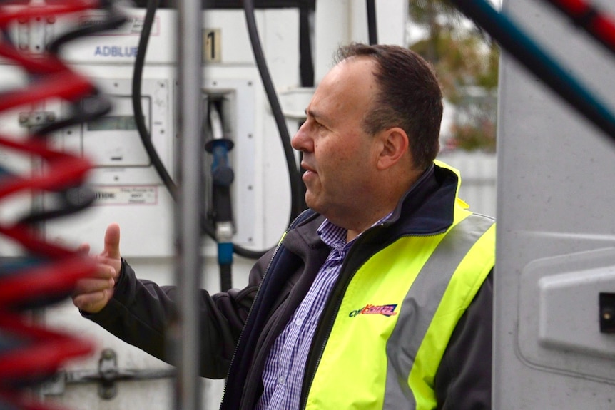 John Di-Losa outside in hi-vis jacket, among petrol bowsers. 