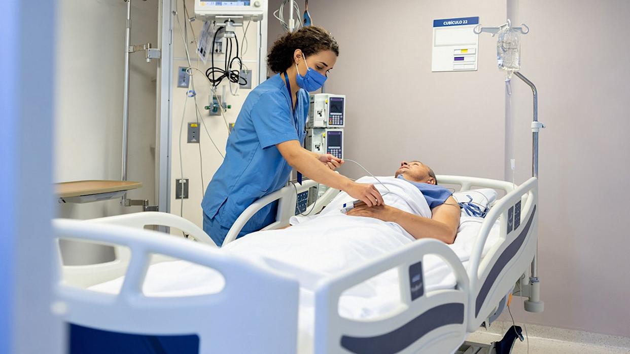 Nurse with mask on placing a pulse oximeter on a patient at the hospital in patient's room.