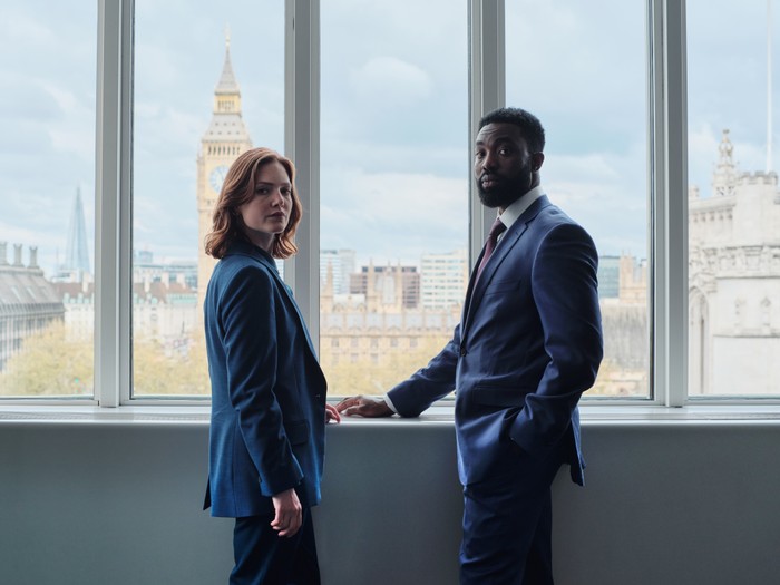 Holliday Grainger and Paapa Essiedu in The Capture season 3, stood by a window with parliament in the background.
