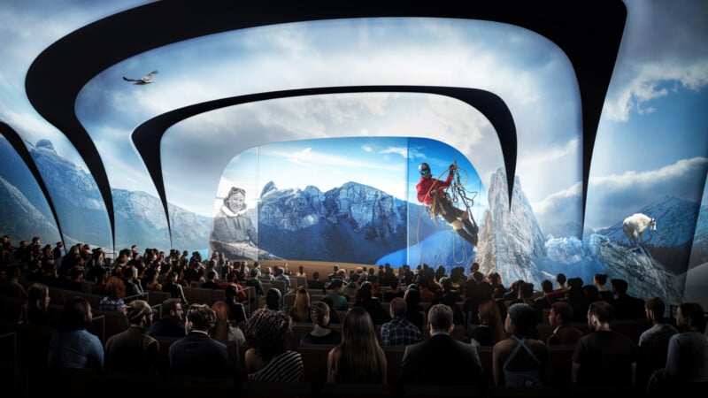 An audience watches an immersive presentation in a theater with curved, futuristic screens displaying mountain scenery, a climber, an eagle, and a bear, creating a dynamic and engaging visual experience.