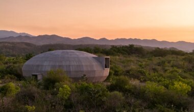 Concrete dome-shaped house in lush green landscape at sunset with mountains in the background