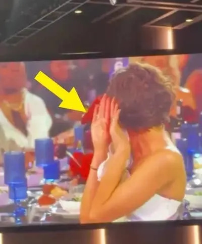 Person at a formal event shielding their face with a hand while seated at a table with blue glasses