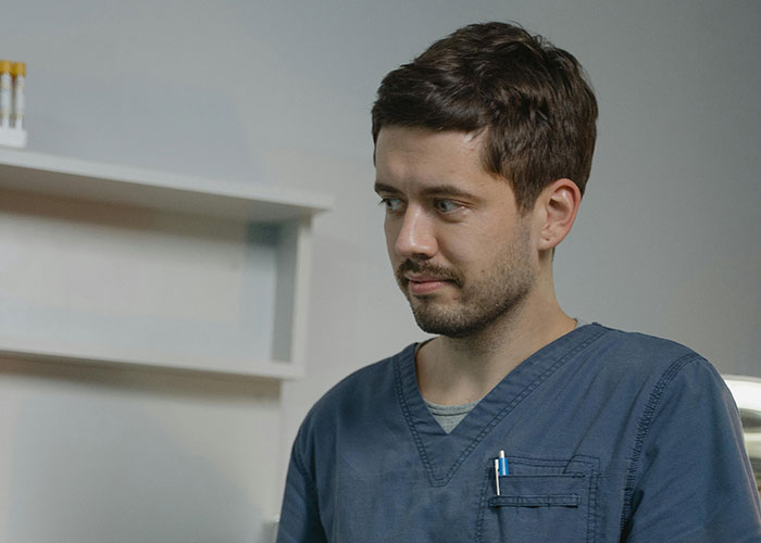 Young medical professional in blue scrubs with pens in pocket, inside a clinical setting exploring medical secrets.