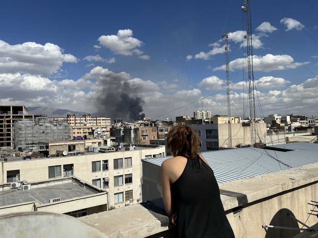 A person watches as plumes of smoke rise over the skyline following explosions on March 1, 2026 in Tehran, Iran. Iran's Supreme Leader, Ayatollah Ali Khamenei, was confirmed killed after the United States and Israel launched a joint attack on Iran on February 28. Iran retaliated by firing waves of missiles and drones at Israel, and targeting U.S. allies in the region.