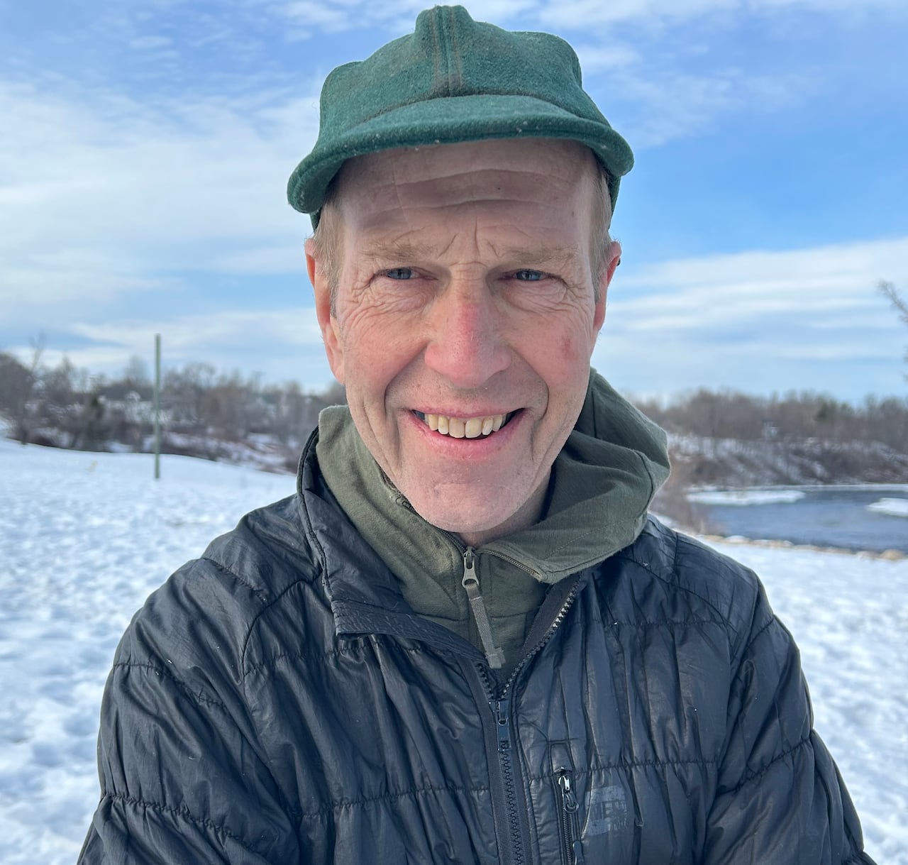 A smiling man wearing a green baseball hat and a black winter coat.