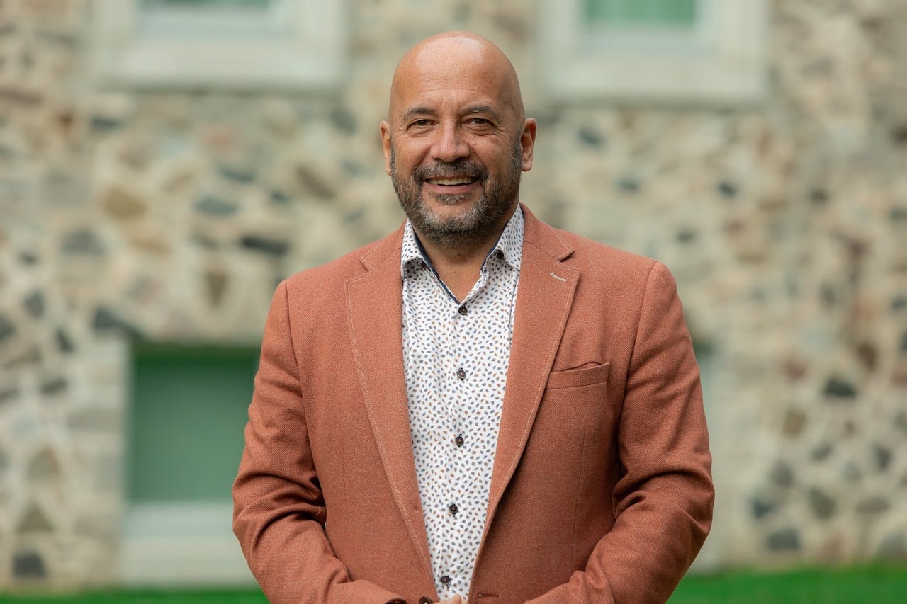 A bald bearded man wearing a burnt orange blazer