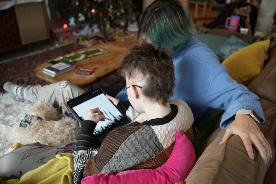 Eliza and Jody sit on the couch in their Squirrel Hill home while Eliza works on an illustration on her iPad.