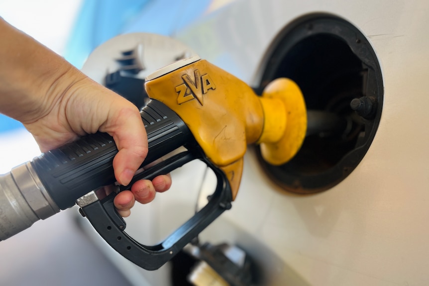 A close up of hand holding a fuel pump at a bowser while filling up car 