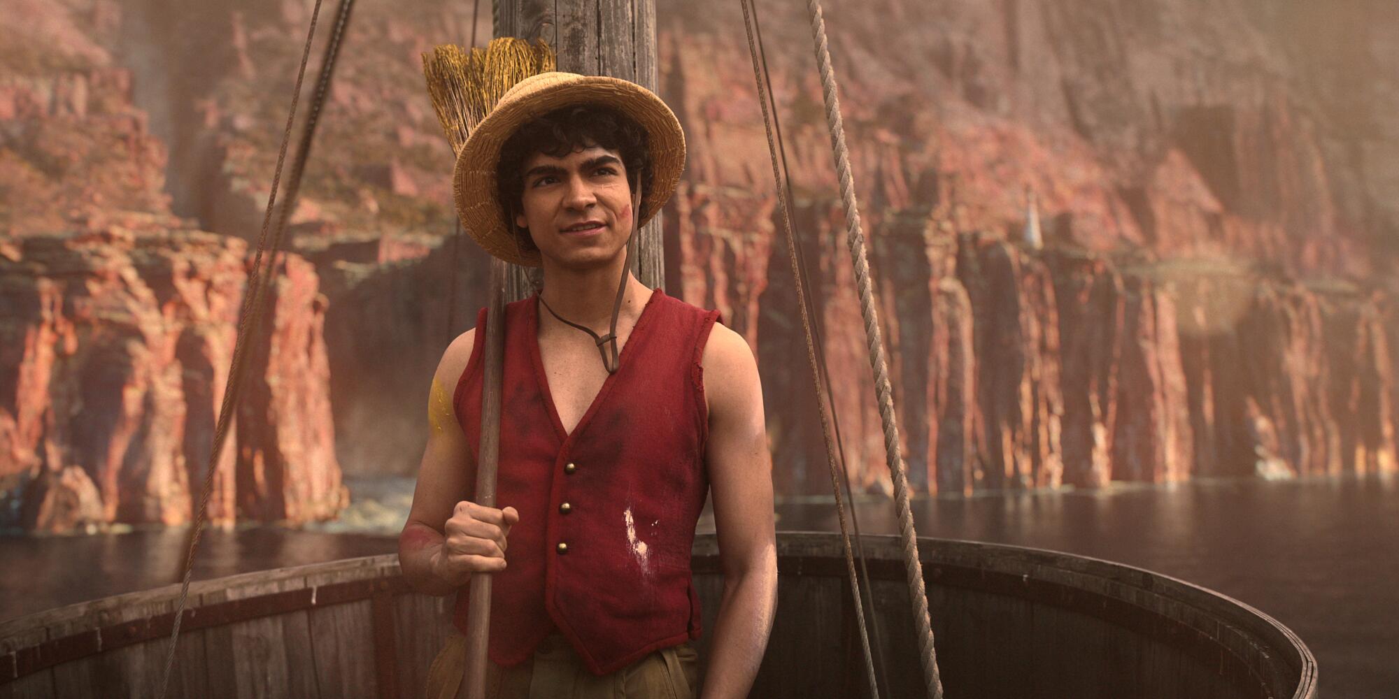 A man in a straw hat and red vest with a broom over his shoulder.