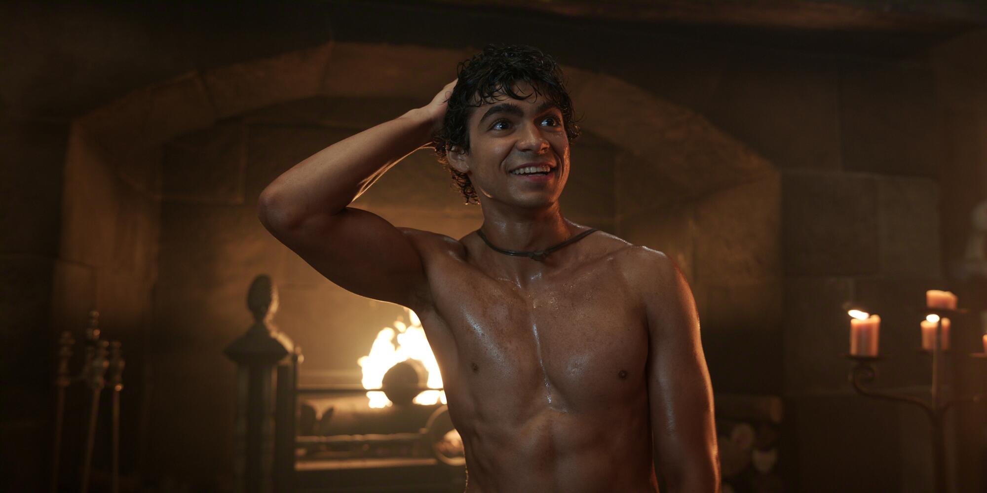 A shirtless man stands with his hand on his head in front of a fireplace.