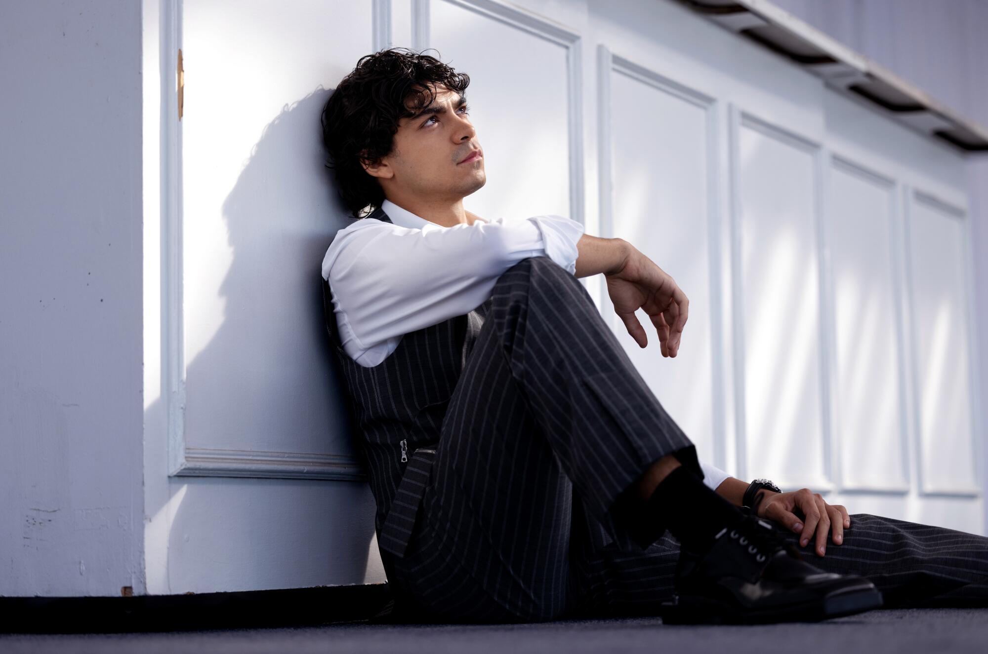 A man in pinstriped outfit leans against a row of white cabinets.