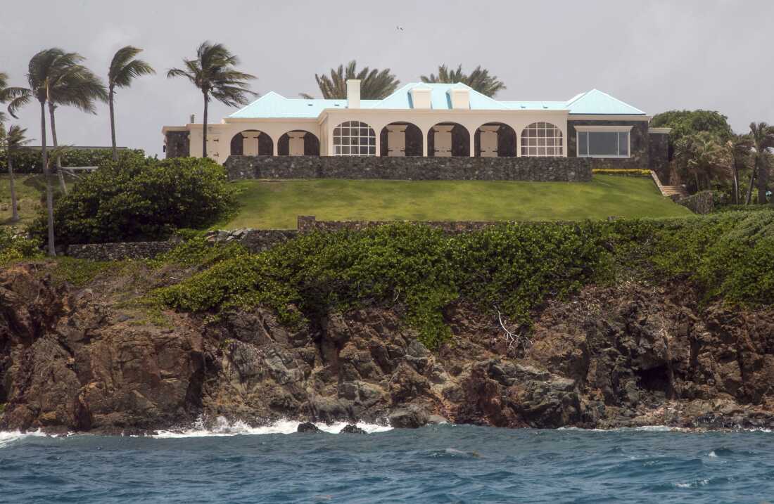 Jeffery Epstein's white mansion on the island of Little Saint James sits above a cliff that meets the blue Caribbean Sea, on July 9, 2019. A few palm trees are on the left side of the frame.