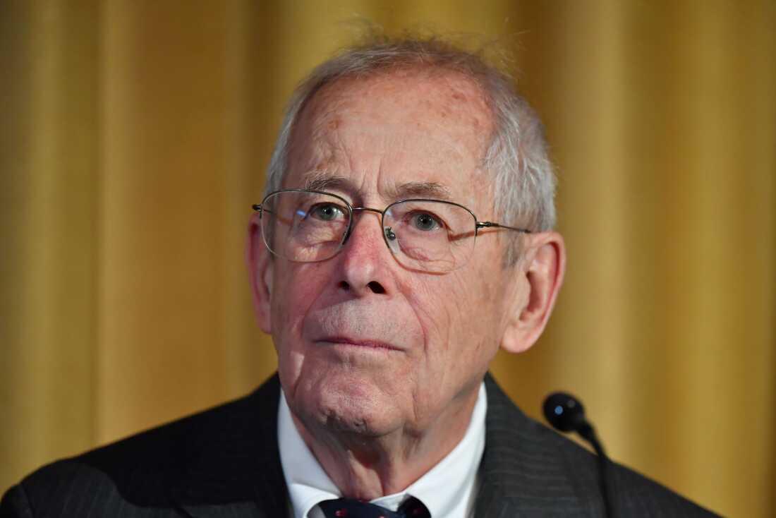 Nobel physics laureate Jim Peebles, photographed from about the shoulders up, attends a news conference at the Royal Swedish Academy of Sciences in Stockholm, Sweden, in 2019. He's wearing a suit and glasses, and he's in front of a microphone.