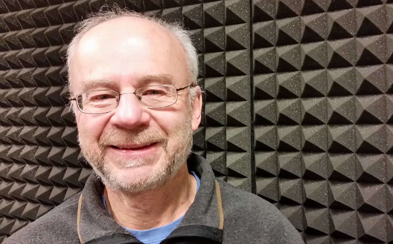 An older man with glasses stands in a radio studio.