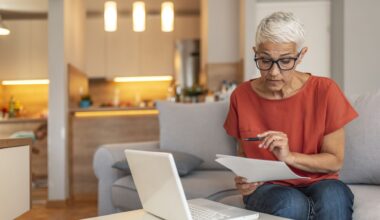 Serious aged woman in eyeglasses checking all bills, calculating expenses.