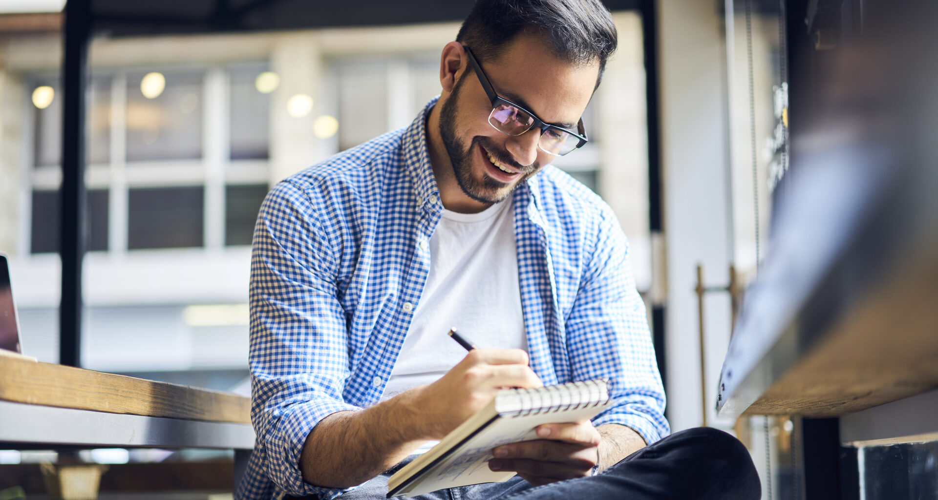 A young man happily writing down money goals, budget and other financial plans inside a business.