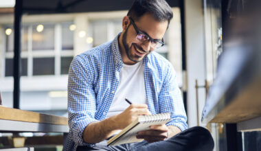 A young man happily writing down money goals, budget and other financial plans inside a business.